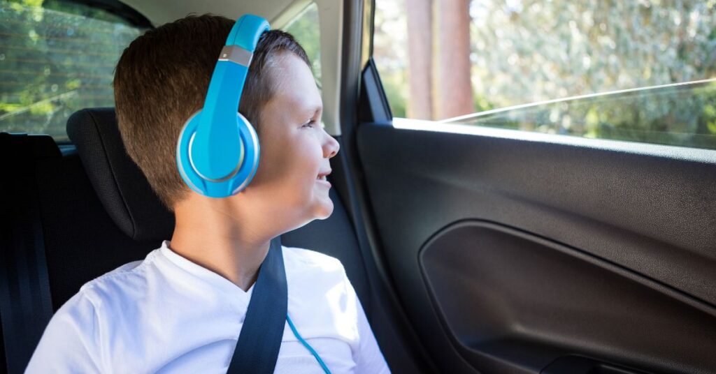 Boy with headphones sitting in car smiling. How can you help your autistic child have more fun on road trips?