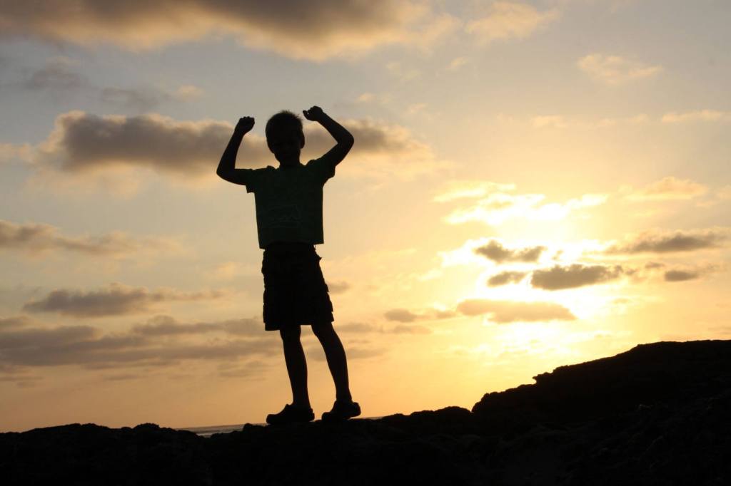 Silhouette of boy raising arms and celebrating victory.