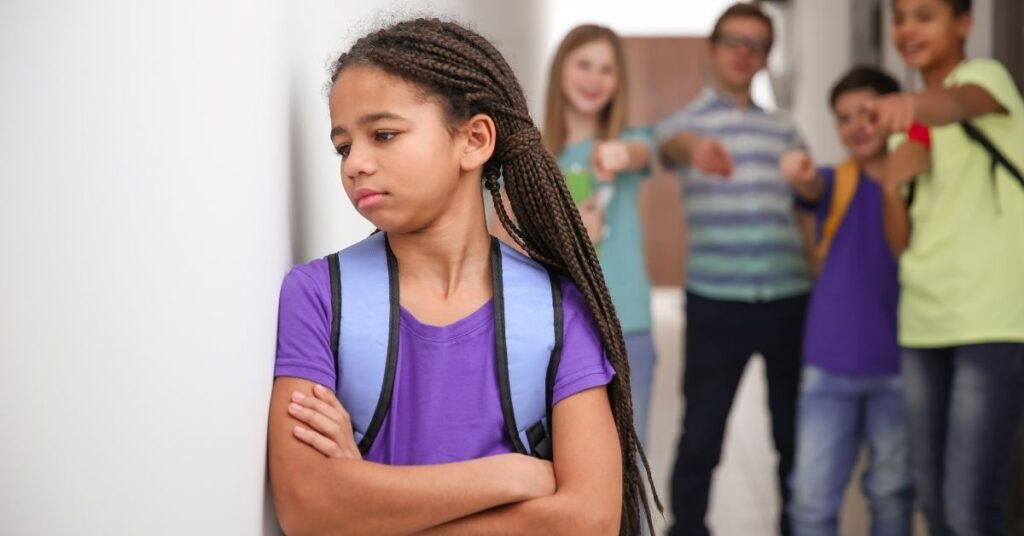 Girl leaning against wall with other kids in the background making fun of her. How to deal with autism stigma.