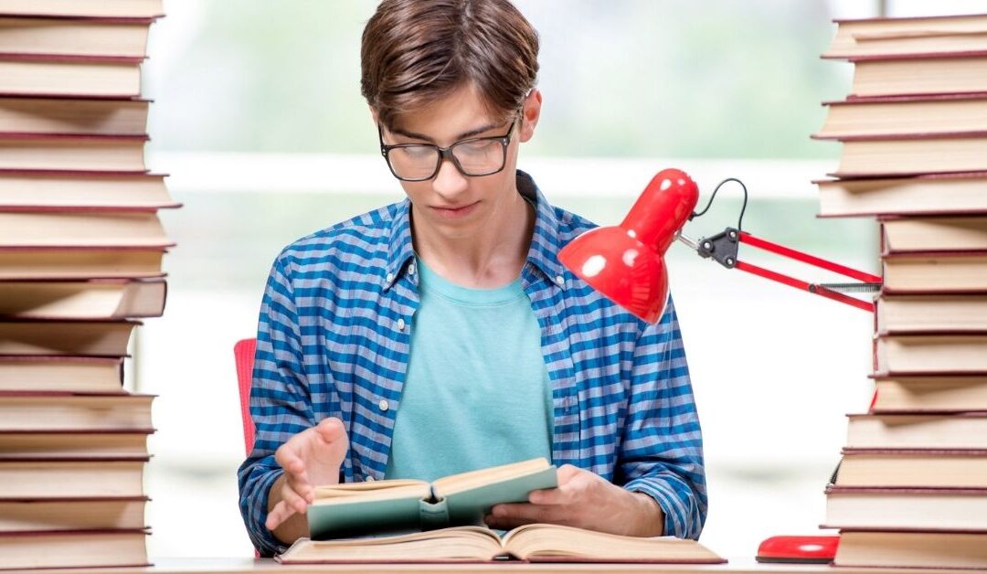 Teenage boy sitting between two tall stacks of books