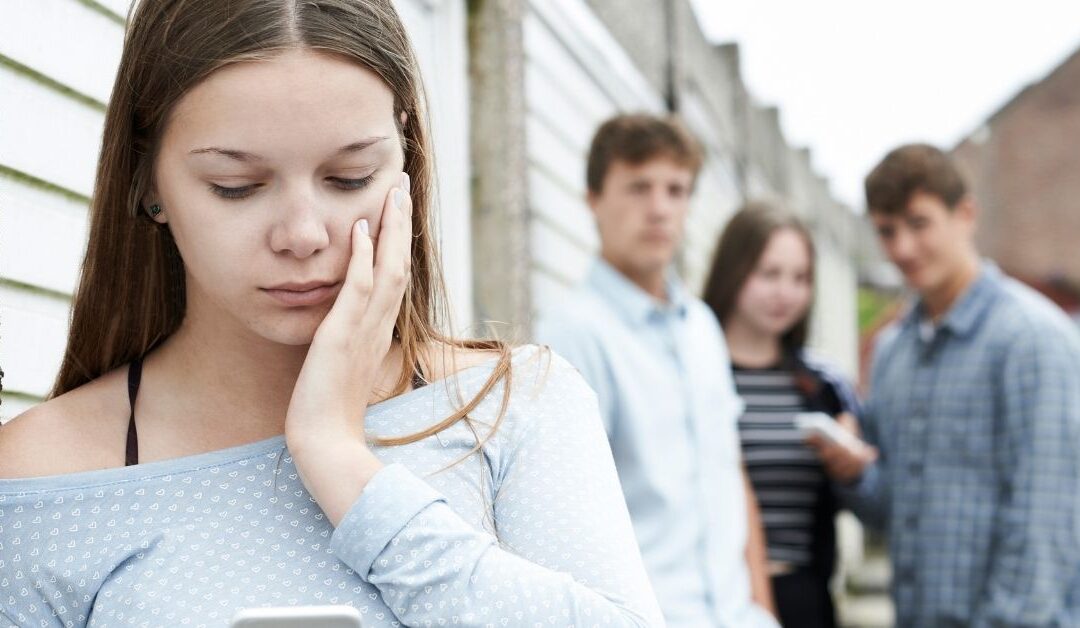 Girl looking at her phone worried with two teens watching behind her.