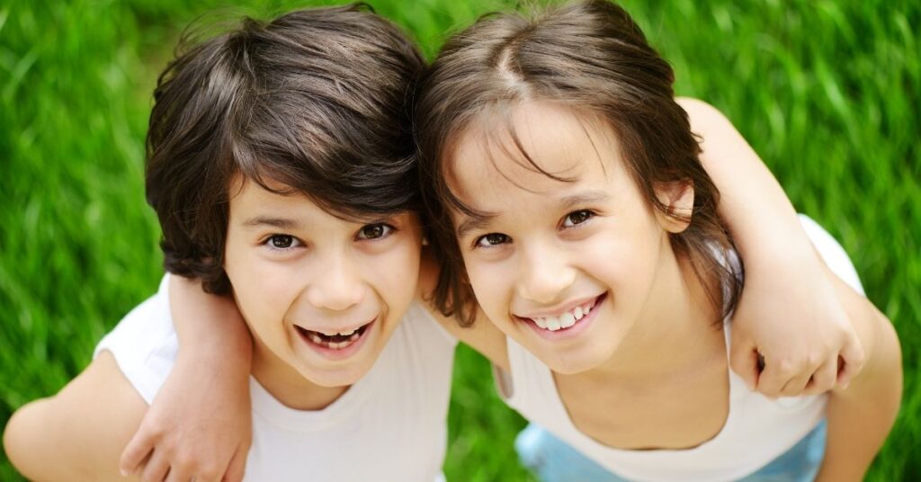 Two girls standing with arms around each other. How to help an autistic child make friends.