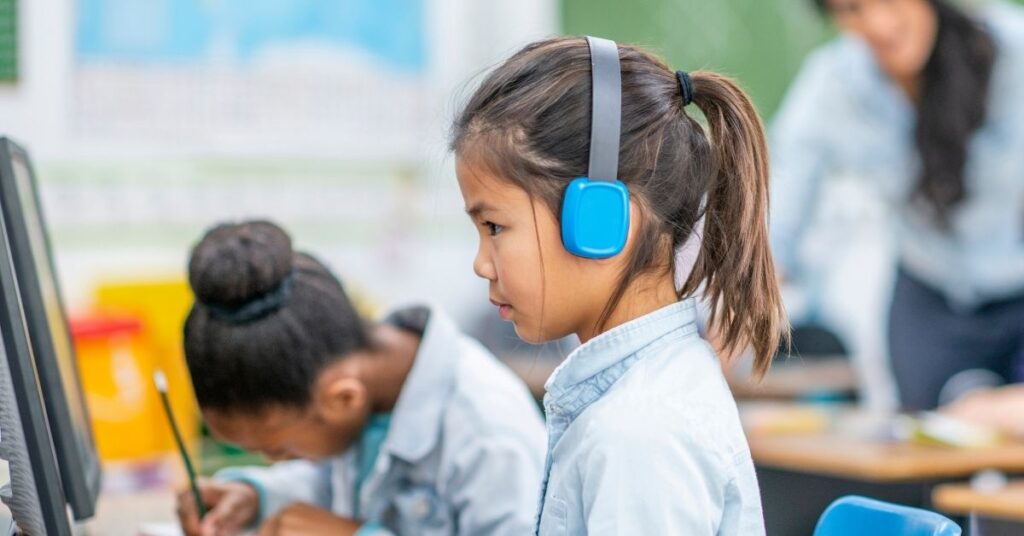 Small girl working at a computer and wearing headphones. How to explain that autism and ADHD are an invisible disability.