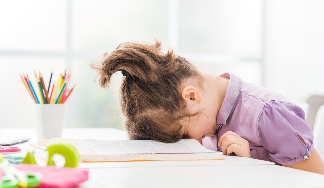 Little girl sitting with head down on table.