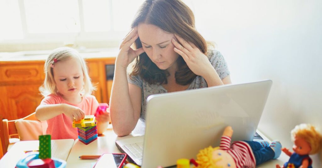 Mom at a computer while little girl sits next to her playing. How to manage stress as a parent of an autistic child.