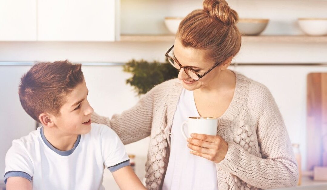 Mom talking to her son with arm around him while he is on the computer.