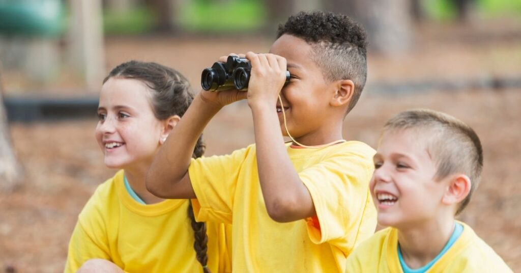 Three kids looking through binoculars. Summer camp offers benefits to children with autism.