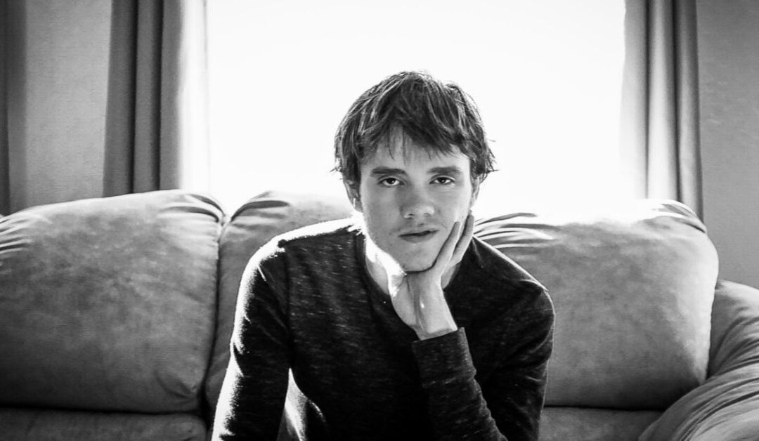 Young adult man sitting on couch with head resting on his hand looking at the camera