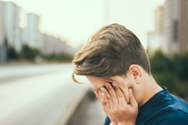 Boy covering his face with his hands. Autistic burnout and emotional exhaustion.