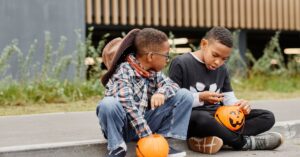 Boys in costume sitting on curb and inspecting their candy from Trick-or-Treating