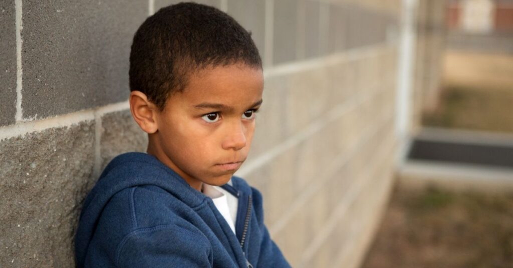 Boy standing against a brick wall, looking upset.