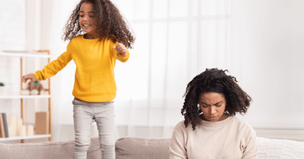 Mom sitting on a couch with daughter jumping on couch. How to overcome parental burnout.